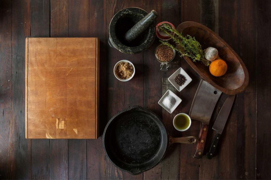 End-grain maple board on dark floorboards beside a cast-iron pan