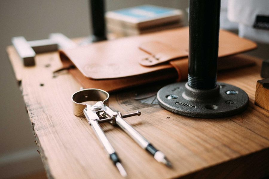Steel drawing compass on a plank workbench beside a tan leather folio