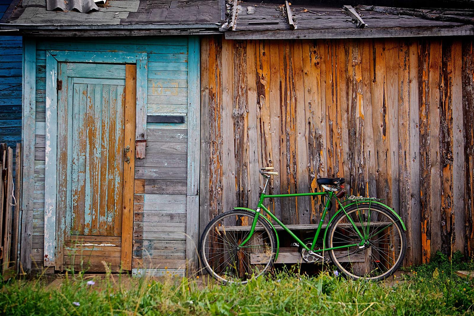 Weathered board shed with a green door and a green bicycle leaning against the boards